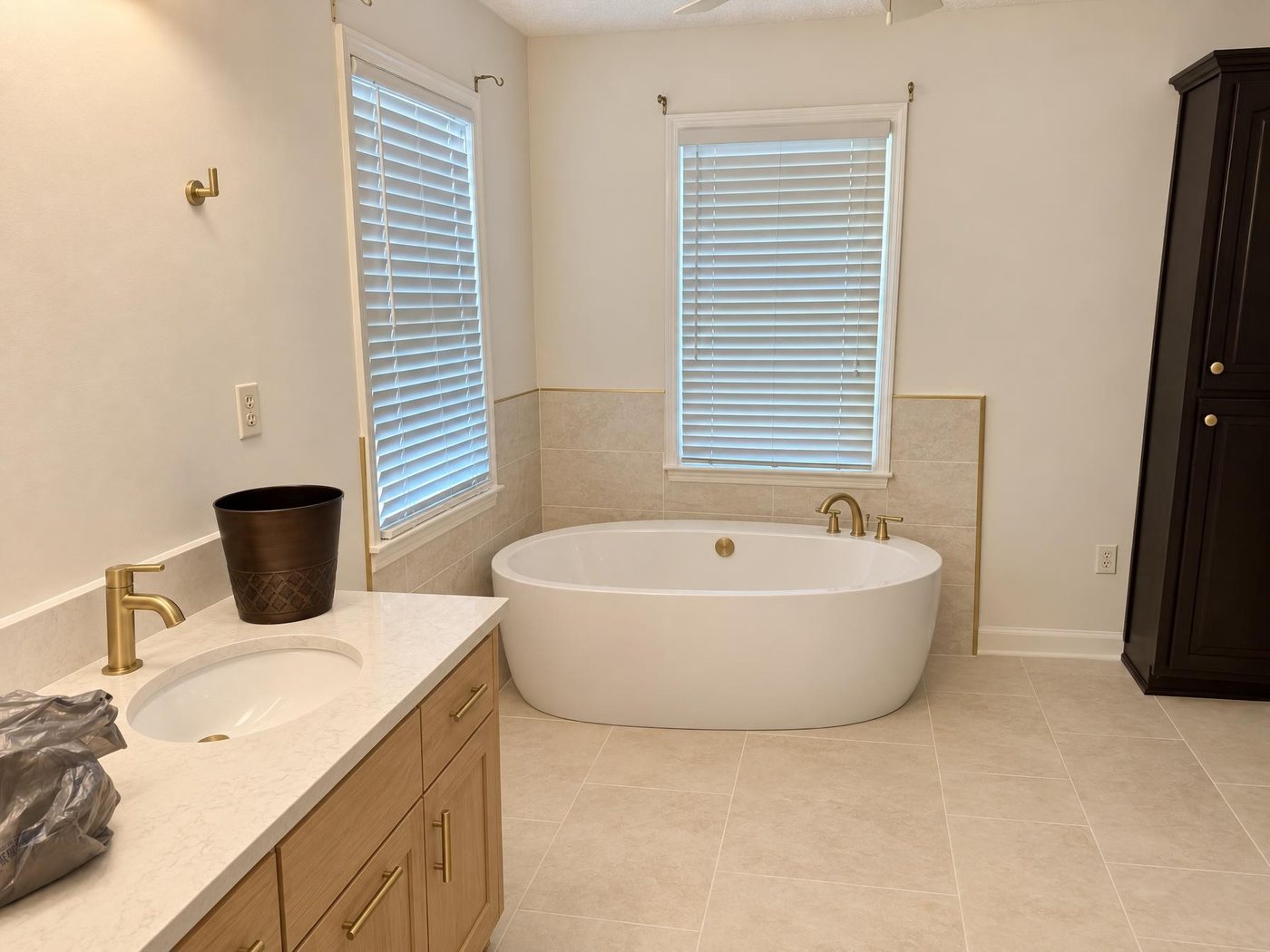The same bathroom redrawn with a freestanding tub, stone-look tile, a white oak vanity and brushed gold fixtures