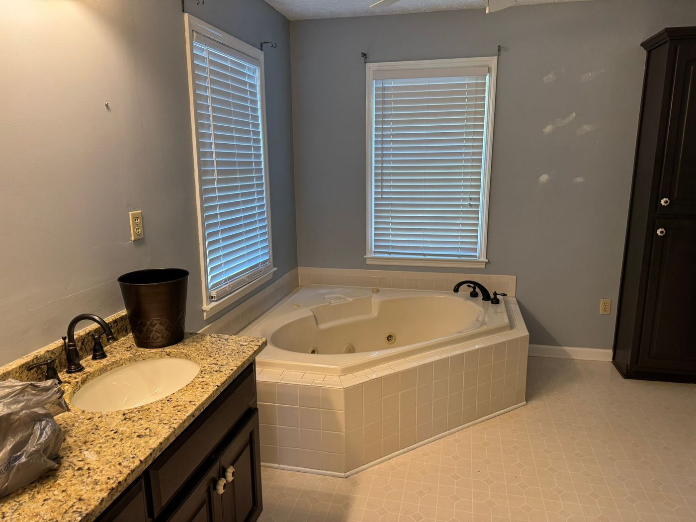 A dated bathroom with a corner jetted tub, a granite vanity and a vinyl floor